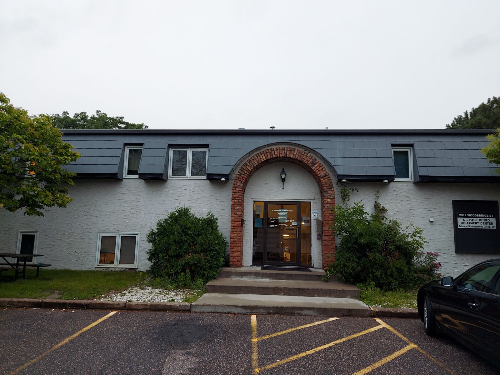 Brick arch entry of a rehab facility with trees and parking