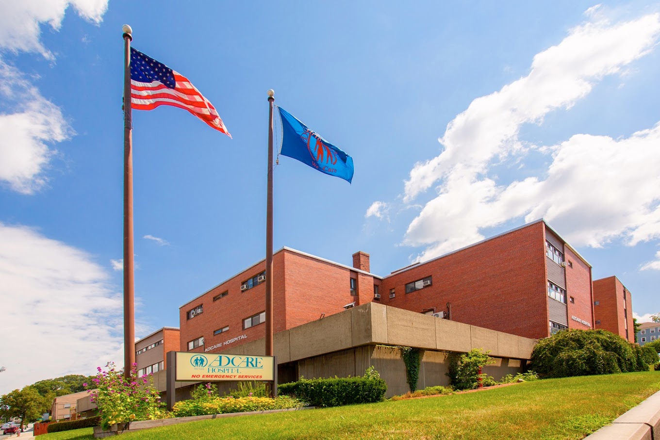 A wide view of AdCare Hospital with flags and a blue sky.