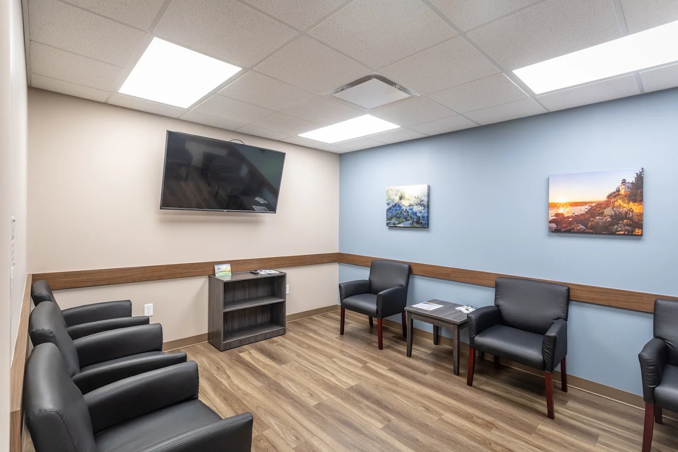 Waiting room with black chairs, wall-mounted TV, and artwork