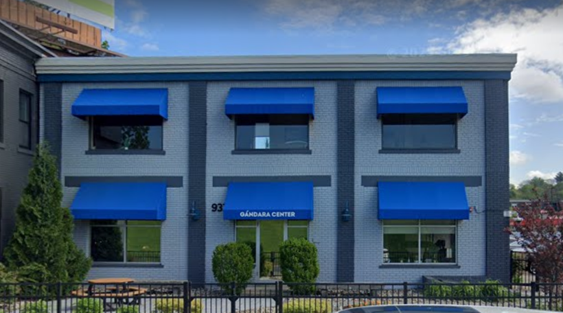 Two-story gray brick building with blue awnings over windows