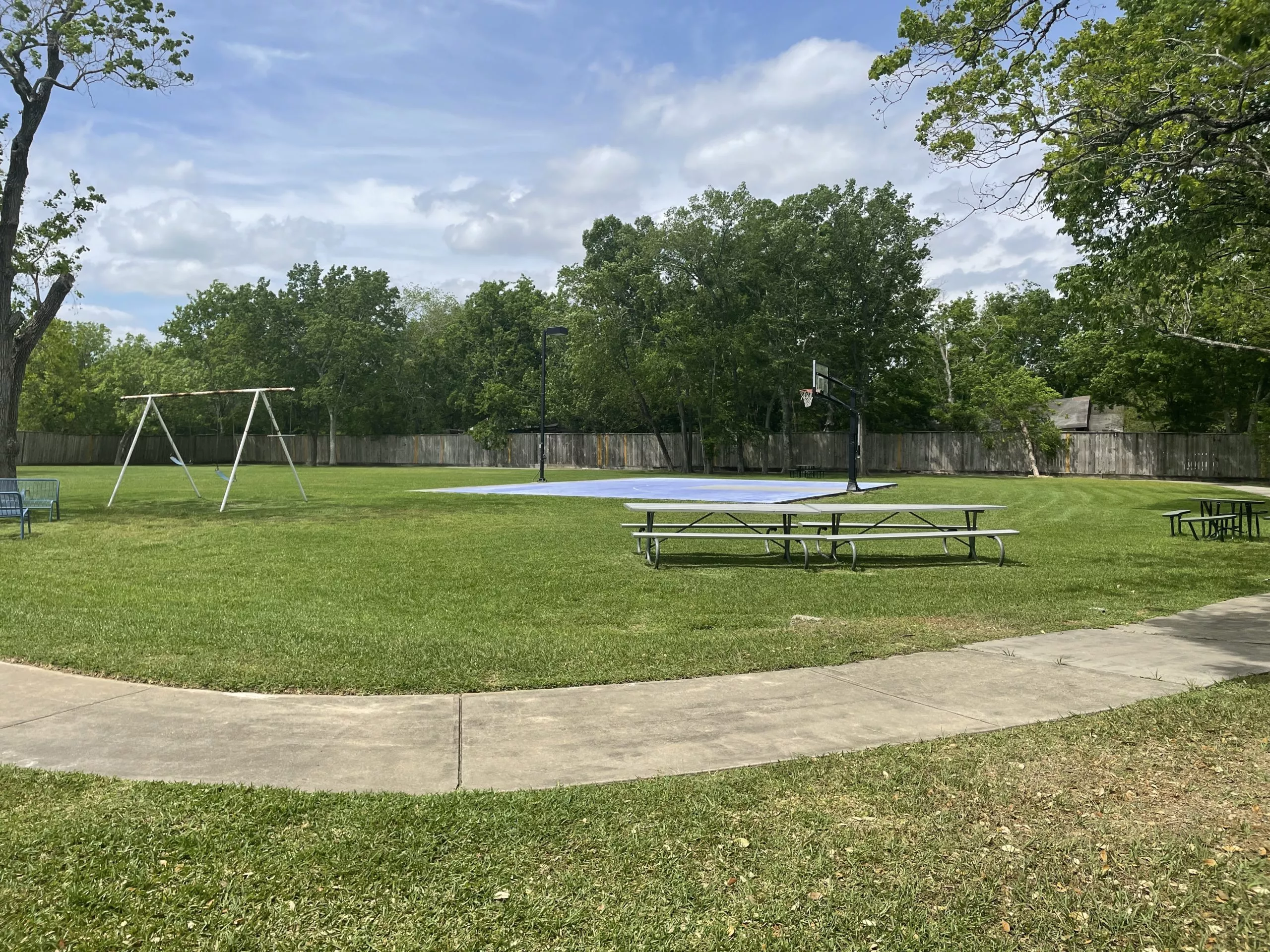 Open grassy yard with basketball court, swings, picnic tables, and trees