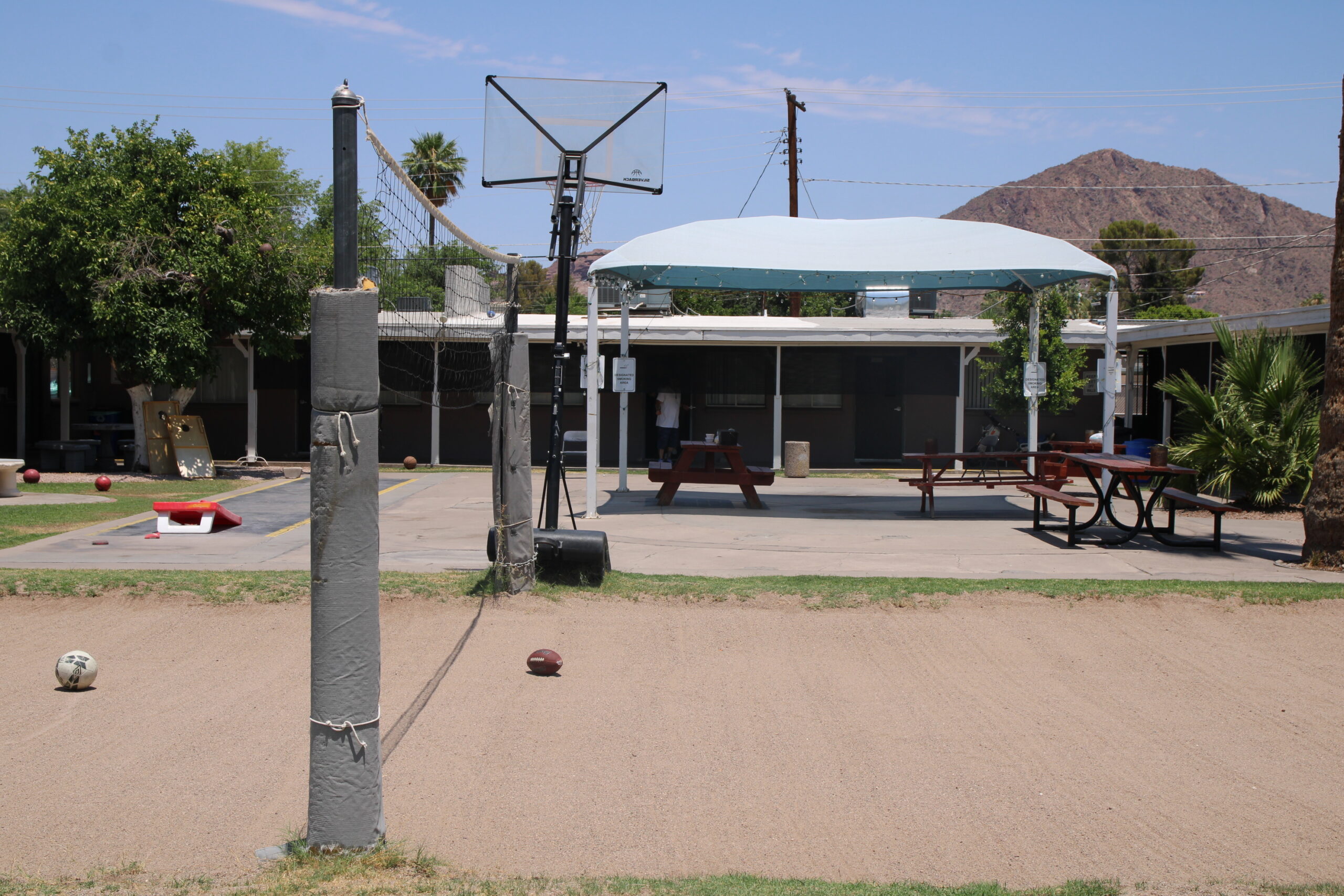 Outdoor area with volleyball net, basketball hoop, cornhole boards, and picnic tables