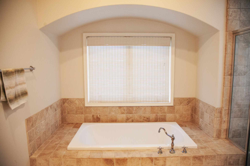Soaking tub set in tiled alcove beneath a wide window