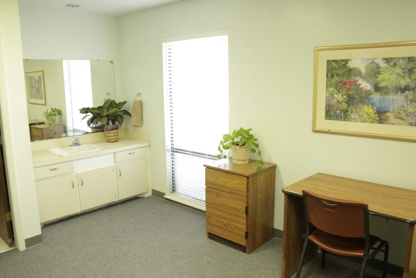 Modest room with sink, desk, dresser, and window.