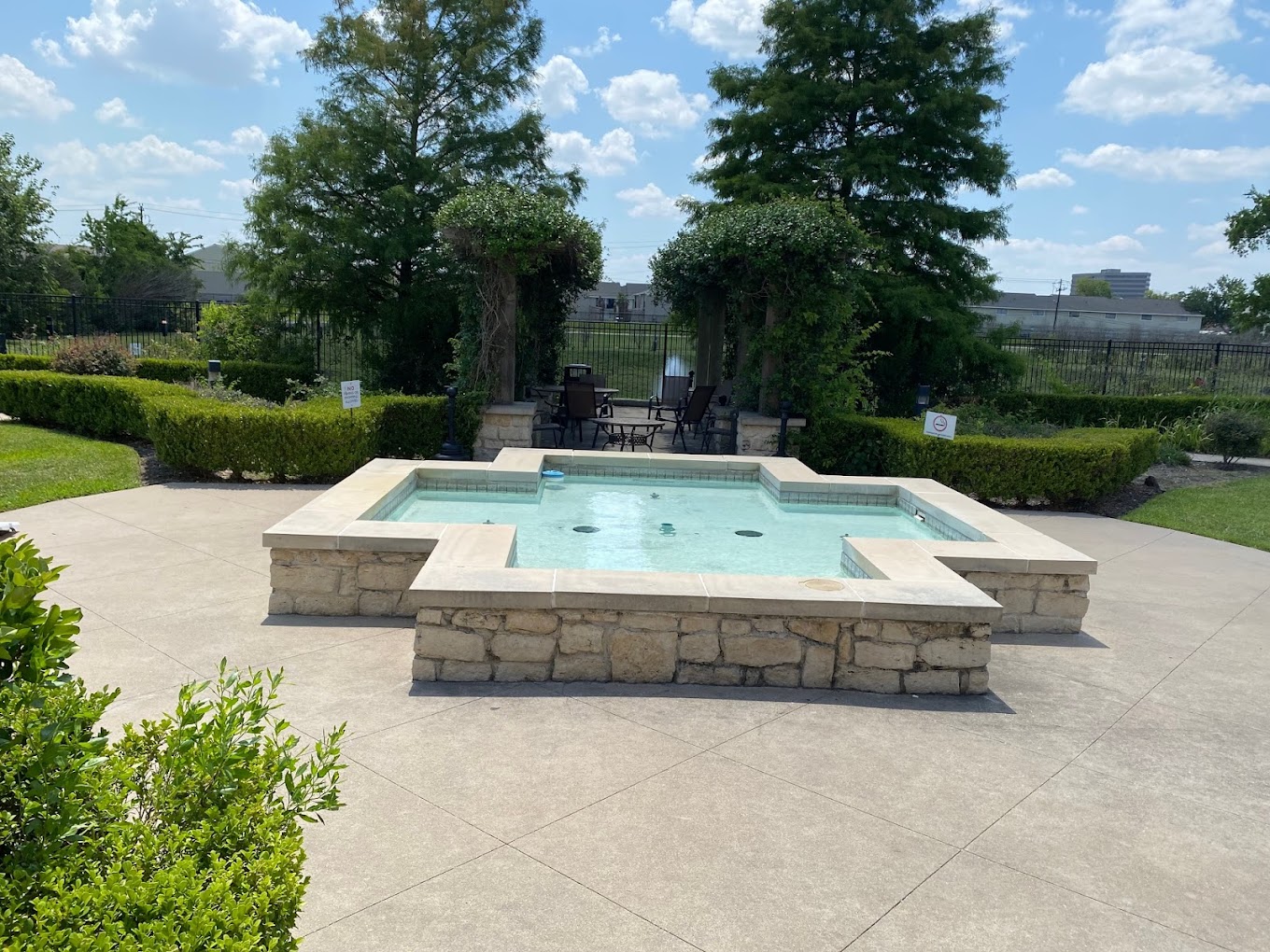 Outdoor area with a fountain around greenery, and a seating area.