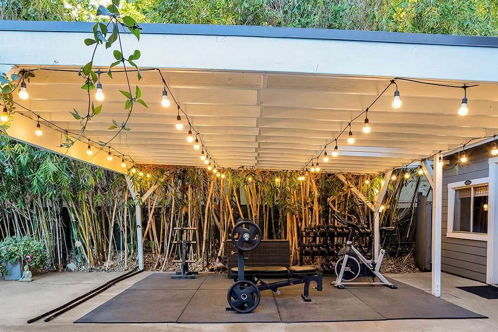 Outdoor fitness area with weights, bike, and string lights under canopy