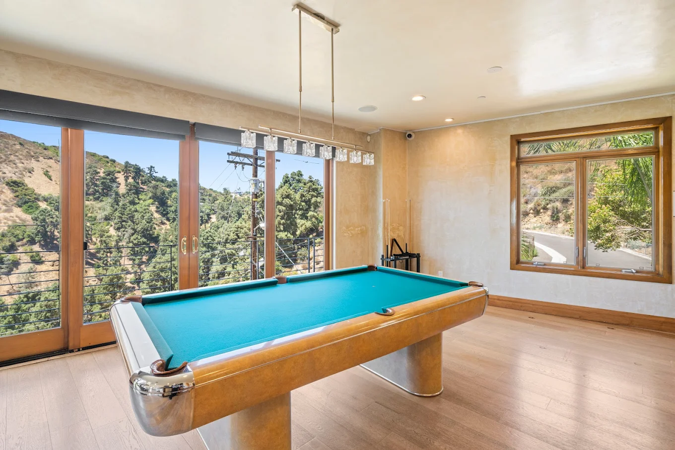 Bright game room with a pool table, floor-to-ceiling windows, and scenic hillside backdrop