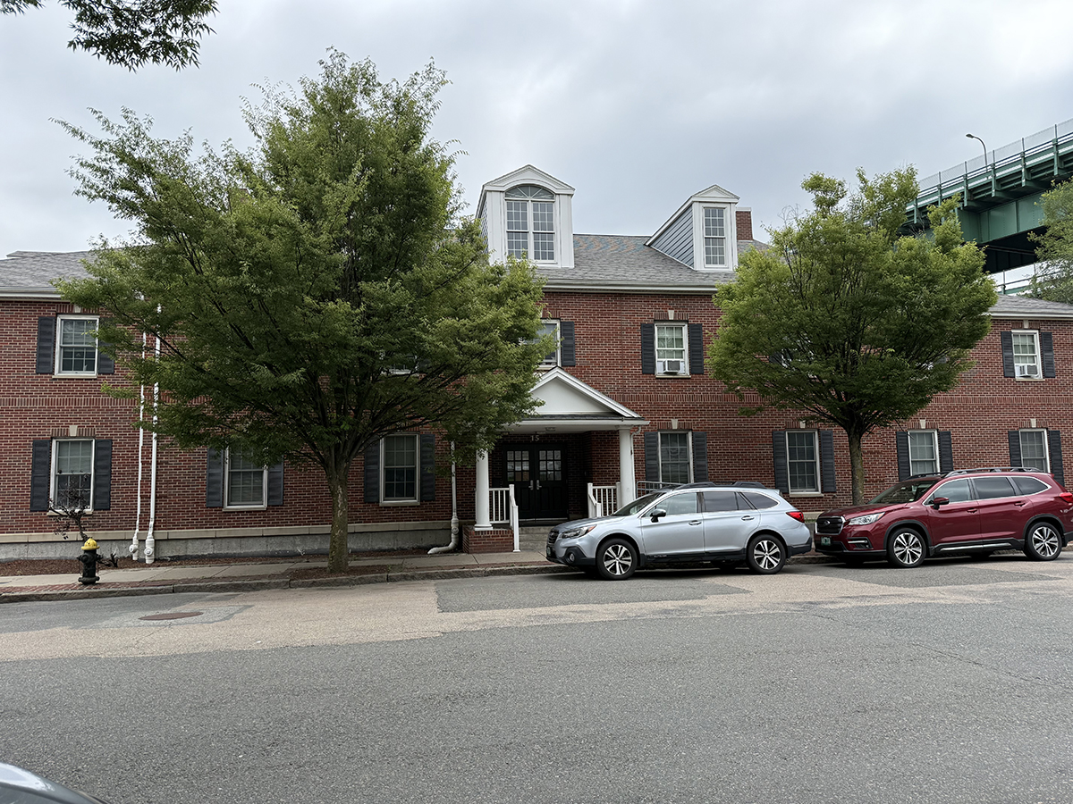 Two-story brick building with dormer windows and parked cars along the street