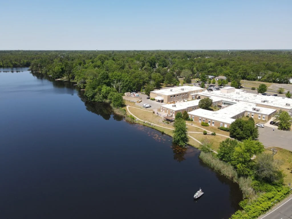 Aerial view of facility buildings beside a lake and trees