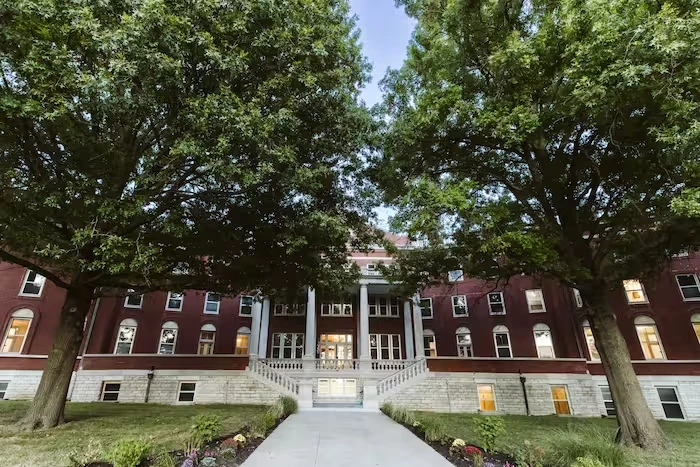 Large brick building framed by mature trees at sunset