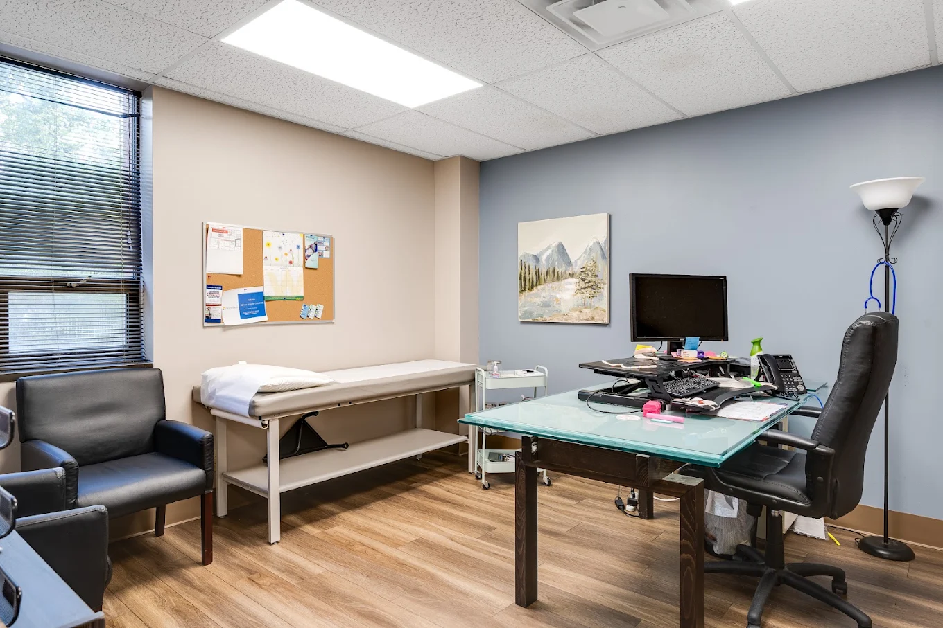 Clinical room with exam table, desk, computer, and chairs