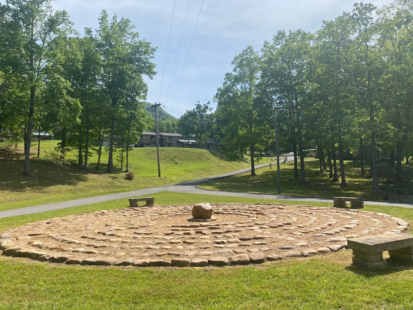 Outdoor stone labyrinth with benches surrounded by trees and lawns