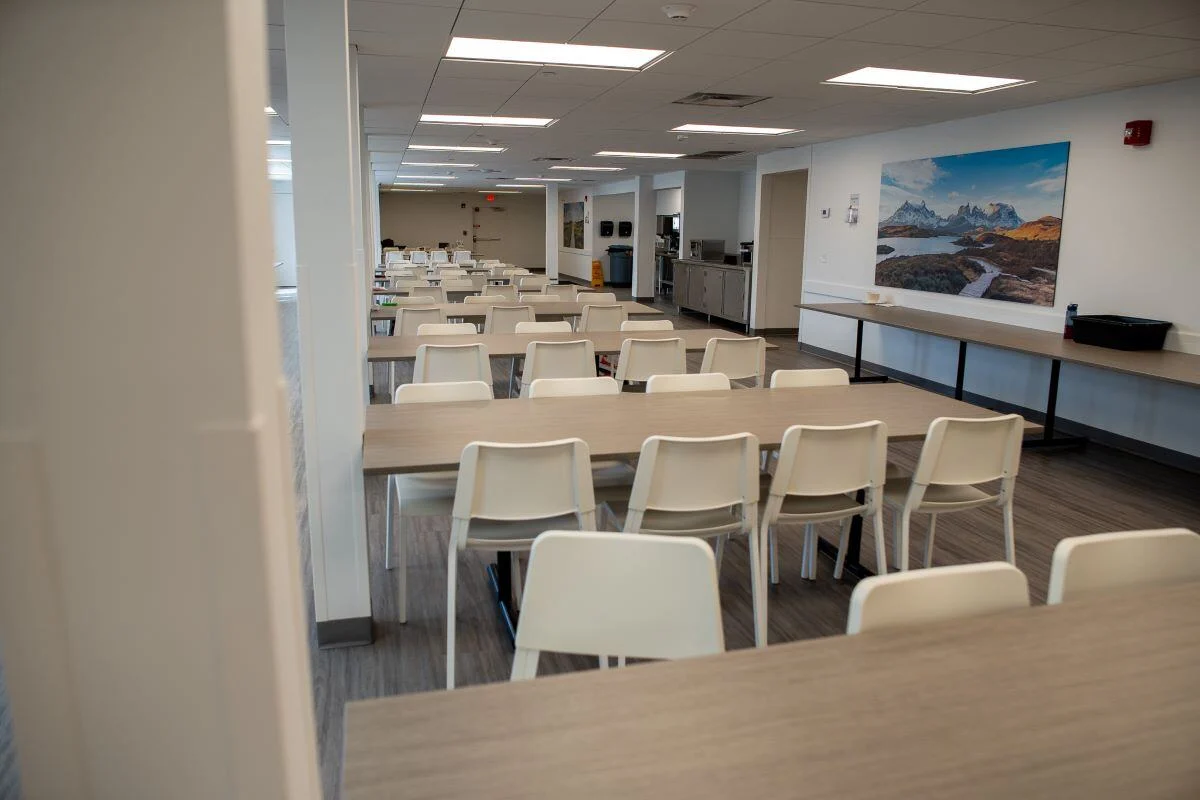 Cafeteria-style dining area with long tables and white chairs