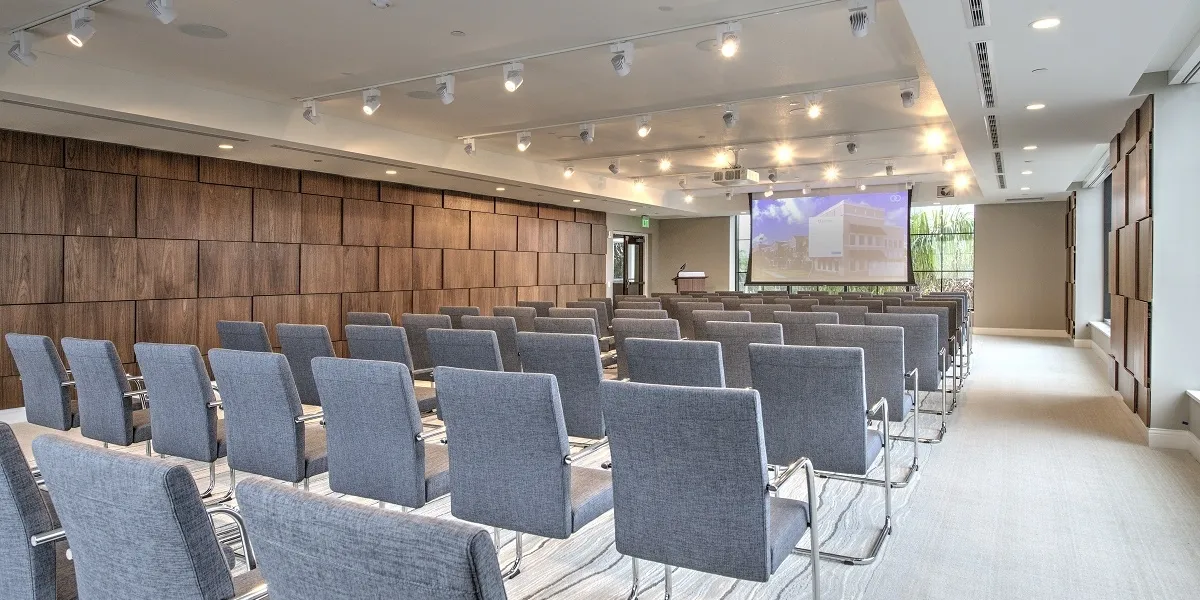 Bright conference room with rows of gray chairs and screen