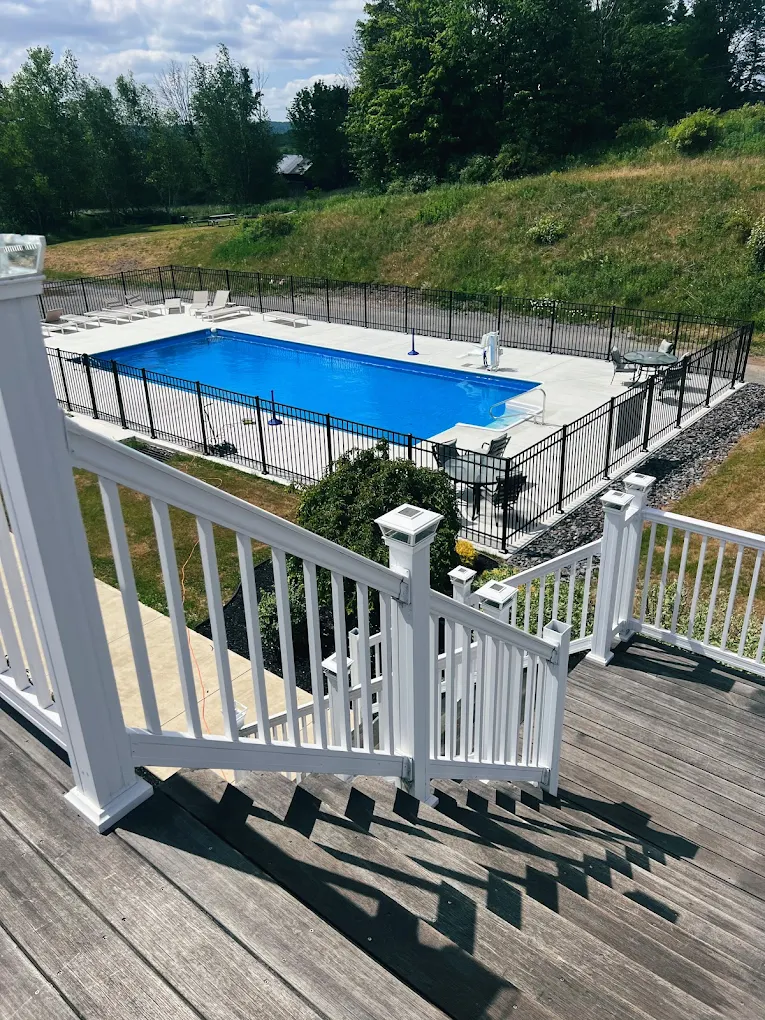 View of outdoor pool from white-railed wooden deck stairs