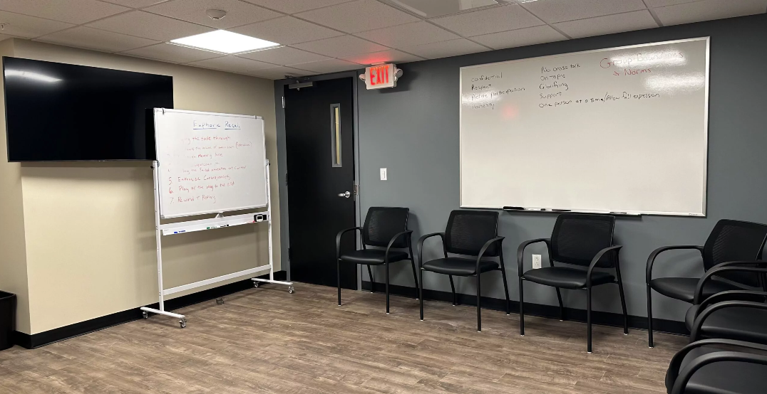 Group therapy room with chairs, whiteboards, and wall-mounted TV.