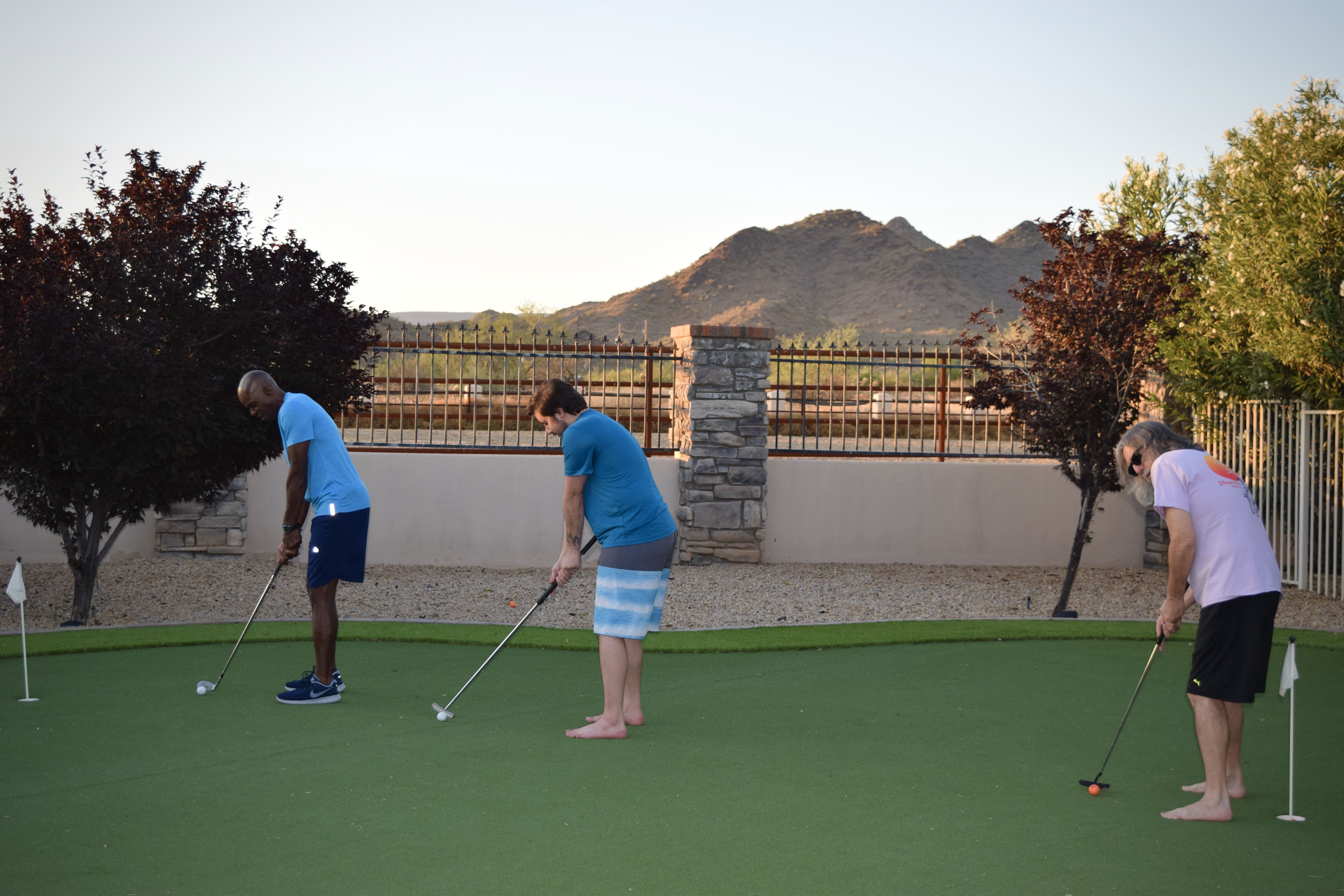 Three men playing mini golf on outdoor putting green