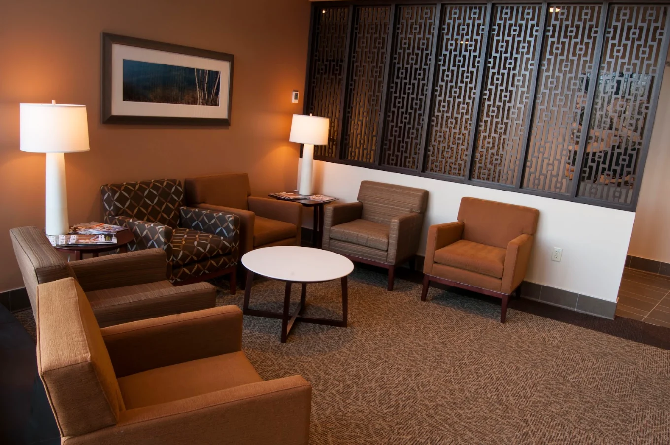 Comfortable lounge area with upholstered chairs, side tables, lamps, artwork, and decorative privacy screens