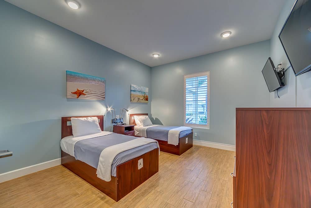 Two twin beds with beach artwork and TV on wall