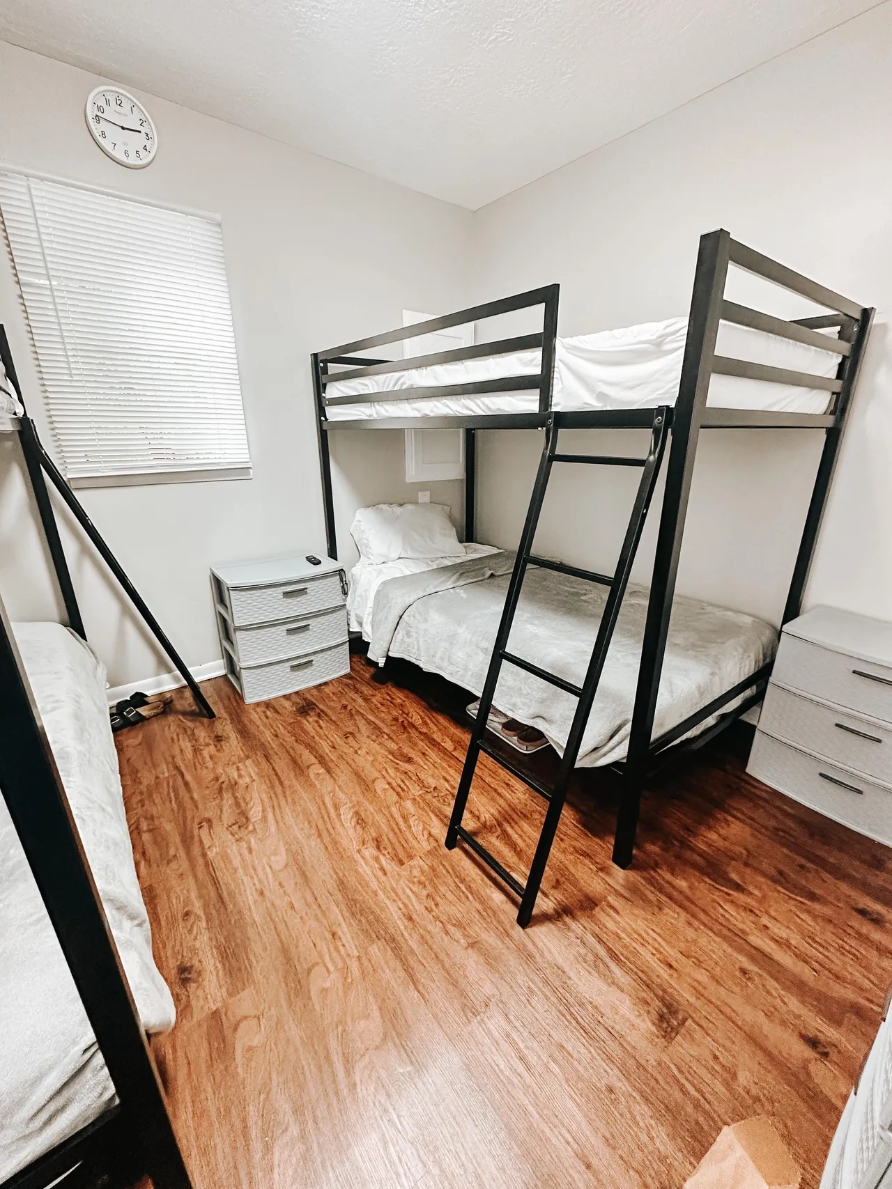 Room with bunk beds, small dressers, and wood flooring