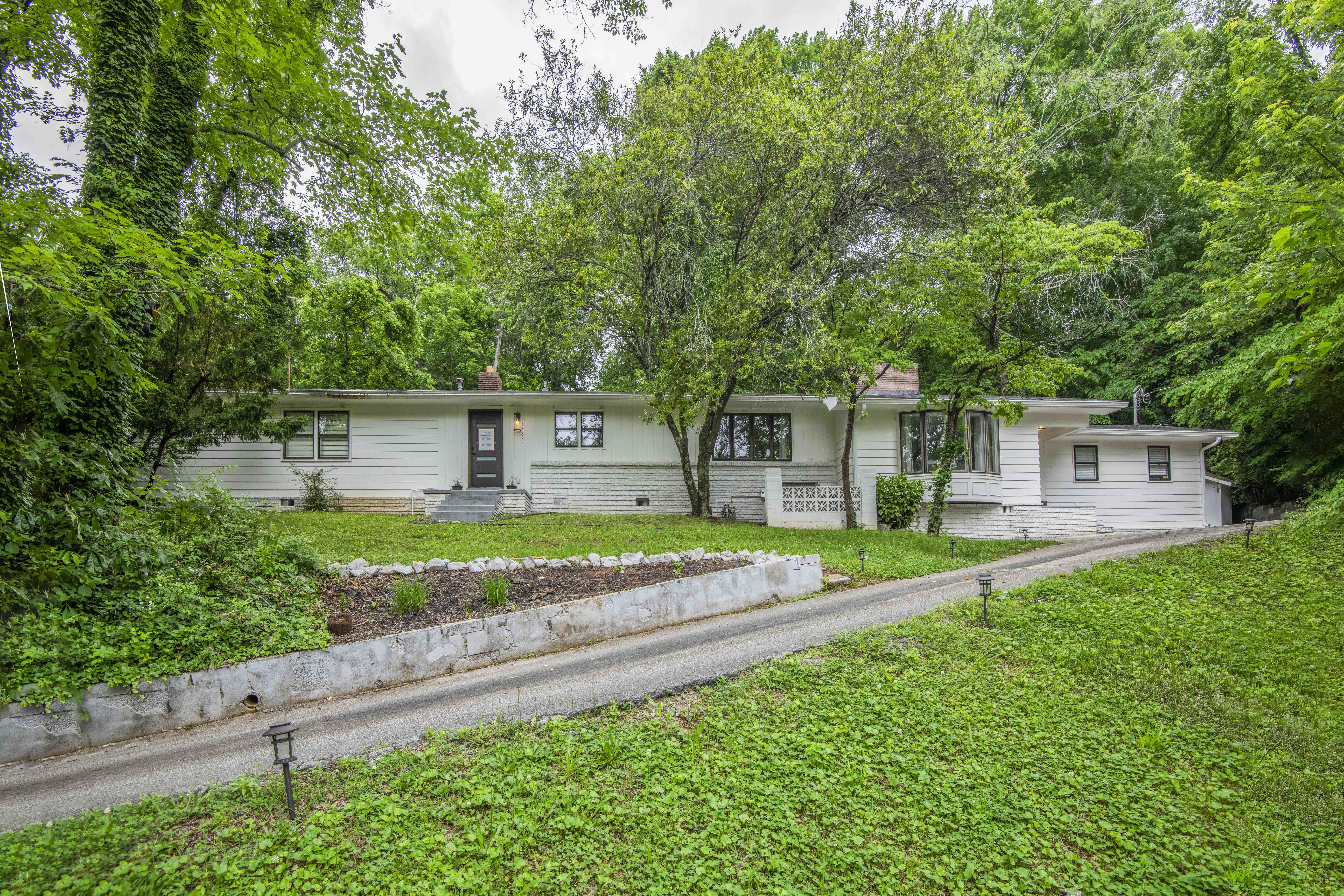 Single-story white house surrounded by lush greenery