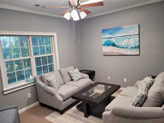 A cozy lounge with gray sofas, a glass coffee table, and ocean artwork.