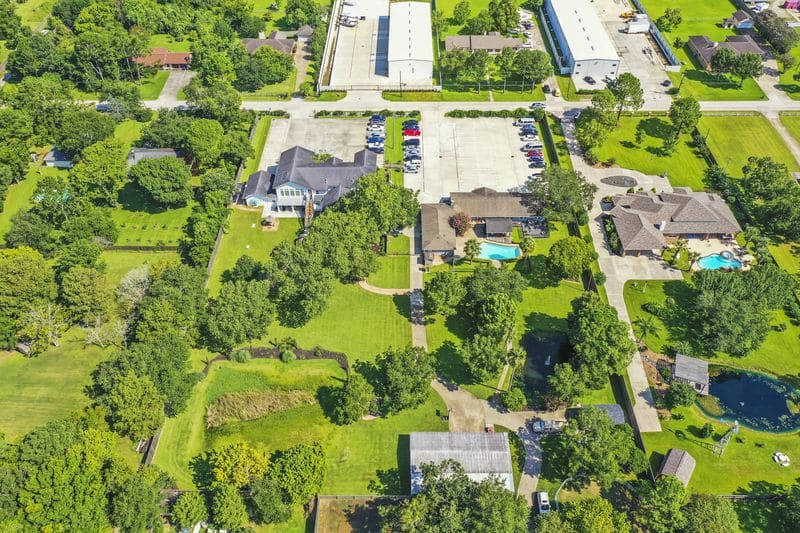 Aerial view of green landscaped property with multiple buildings, driveways, and parking areas