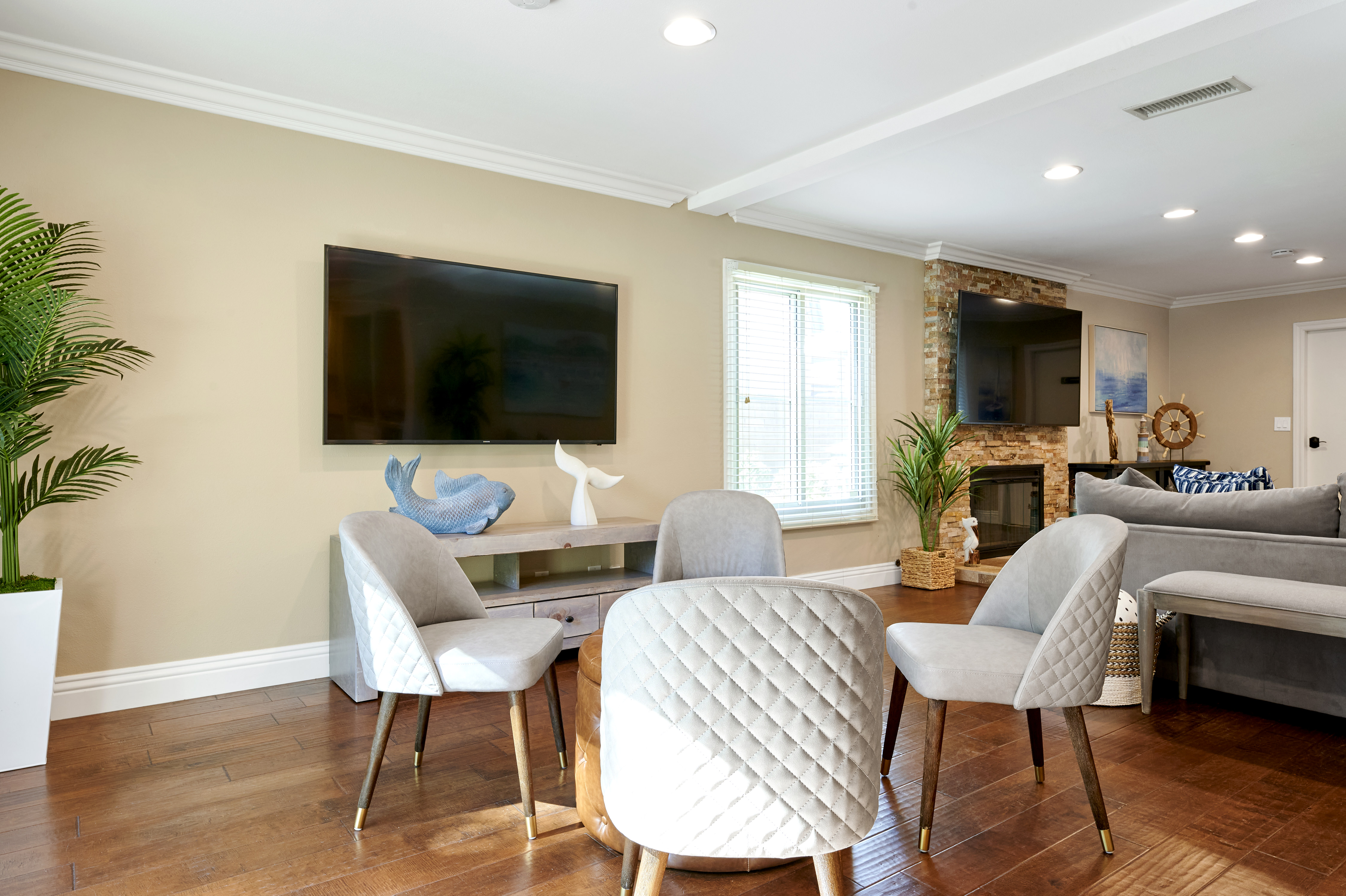 A modern living space with comfortable seating, a wall-mounted TV, and tasteful coastal decor, complemented by natural light and greenery.